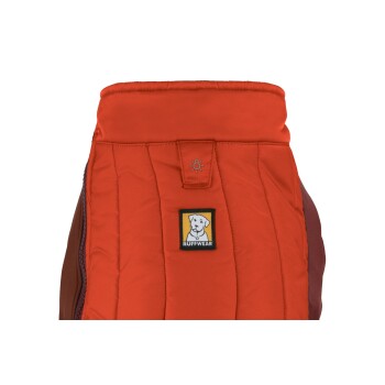 Eine Nahaufnahme einer roten Hundejacke mit einem gesteppten Design und einem schwarzen und gelben "Ruffwear"-Logo mit einer Hundedarstellung.