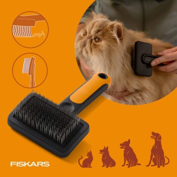 Fiskars-Slicker-Bürste mit orangem Griff und Metallstiften, gezeigt beim Bürsten einer langhaarigen Katze; 'FISKARS'-Logo sichtbar