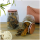 Zwei Glasbehälter gefüllt mit Haustierleckereien, einer umgekippt und verschüttet Leckereien, auf einem Holztisch mit einem Seilspielzeug und einem rosa Kissen im Hintergrund.