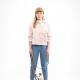 Eine Frau in einer hellrosa Jacke und blauen Jeans steht mit einem kleinen Hund an der Leine, vor einem schlichten weißen Hintergrund.