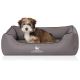 Ein kleiner, flauschiger Welpe sitzt bequem in einem grauen Hundebett mit einem gesteppten Design, mit dem Logo 'KNUFFELWUFF'.