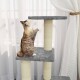 Eine verspielte getigerte Katze, die auf einem grauen Katzenbaum mit zwei Plattformen und sisalumwickelten Pfosten nach oben greift, in der Nähe von durchsichtigen weißen Vorhängen.