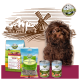 Ein kleiner brauner Hund sitzt neben Tierfutterprodukten: einer Tüte 'FREILAND-HAPPEN' und Dosen 'FREILAND-MENU' (Huhn) und 'HEIDE-MENU' (Lamm).