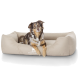 Ein brauner und weißer Australian Shepherd Hund liegt auf einem beigen Hundebett, auf dem das Logo "KNUFFELW" sichtbar ist.