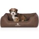Ein kleiner, flauschiger Hund sitzt bequem in einem braunen Hundebett mit strukturiertem Innenraum, mit dem Logo "KNUFFELWUFF."