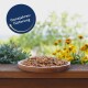 Eine Holzschüssel mit insektengestütztem Haustierfutter auf einer Holzoberfläche, umgeben von Grünpflanzen und gelben Blumen, mit einem blauen Etikett "Ganzjahresfütterung."