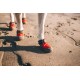 Nahaufnahme von Hundepfoten, die leuchtend rote und graue Schutzschuhe auf sandigem Boden tragen, die das Design des Schuhwerks zeigen.