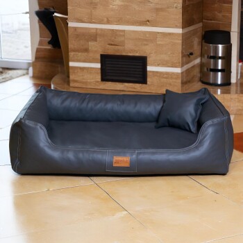 Schwarzes Lederhaustierbett mit Kissen, auf gefliestem Boden nahe einer Steinmauer und einem Mülleimer platziert.