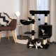 Eine gemütliche Wohnzimmer-Szene mit einem schwarzen Katzenbaum, auf dem drei schildpattfarbene Katzen faulenzen, einem modernen Stuhl mit einem gemusterten Kissen und einer Lampe.