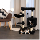 Eine gemütliche Wohnzimmer-Szene mit einem schwarzen Katzenbaum, auf dem drei schildpattfarbene Katzen faulenzen, einem modernen Stuhl mit einem gemusterten Kissen und einer Lampe.