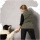 Eine Frau in einer grünen Weste interagiert mit einem großen, flauschigen schwarz-weißen Hund, der seine Pfote hebt.