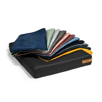 Ein schwarzes Haustierbett mit einem Stapel bunter, weicher Decken in verschiedenen Farbtönen, darunter Blau, Grün, Grau und Burgunder.