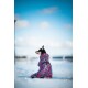 Ein schwarz-brauner Hund, der einen bunten, pink-lila gemusterten Wintermantel trägt, sitzt im Schnee und schaut zur Seite.