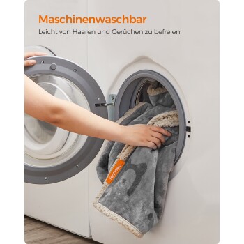 Eine Person fügt eine graue, flauschig umrandete Tierdecke mit der Aufschrift 'Maschinenwaschbar' in eine Waschmaschine hinzu.