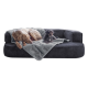 Zwei Hunde ruhen sich auf einem plüschigen, dunkelgrauen Sofa aus, das mit einer weichen, hellgrauen Decke bedeckt ist.