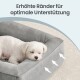 Kleiner weißer Hund in grauem Hundebett mit Pfeilen an der erhöhten Kante; Text 'Erhöhte Ränder für optimale Unterstützung'.