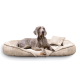 Ein grauer Weimaraner-Hund liegt auf einem plüschigen, beigen Haustierbett mit einem kleinen Kissen und schaut aufmerksam in die Kamera.