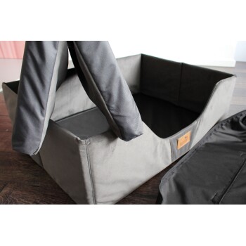 Ein graues Haustierbett mit abnehmbarem Bezug, das ein Lederetikett auf einem Holzboden zeigt.