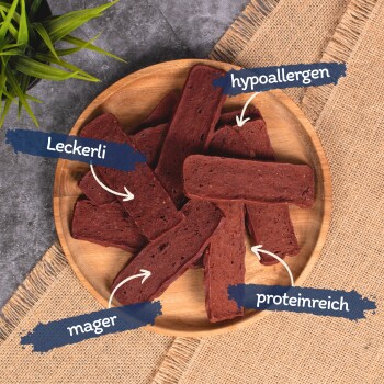 Ein Holzbrett gefüllt mit rechteckigen Hundeleckerlis, beschriftet mit den Texten: "Leckerli", "hypoallergen", "mager" und "proteinreich."