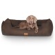 Ein braunes Hundebett mit plüschiger, weicher Textur, mit einem Hund, der bequem darauf liegt, und einem Lederetikett mit Logo.