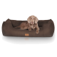 Ein braunes Hundebett mit plüschiger, weicher Textur, mit einem Hund, der bequem darauf liegt, und einem Lederetikett mit Logo.