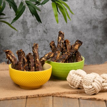 Zwei Schalen gefüllt mit Hundeleckerlis, eine gelbe und eine grüne, auf Jute mit einem Seilspielzeug daneben platziert.