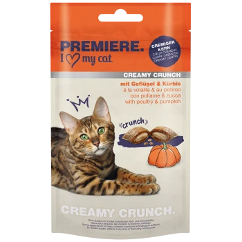 A Bengal cat with green eyes rests beside a package of "Premiere I Love My Cat Creamy Crunch" treats, featuring poultry and pumpkin.