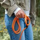 Hand hält eine knallorangefarbene Seilleine mit schwarzem Karabiner, Person in Jeans und beiger Jacke im Freien.