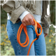 Hand hält eine knallorangefarbene Seilleine mit schwarzem Karabiner, Person in Jeans und beiger Jacke im Freien.