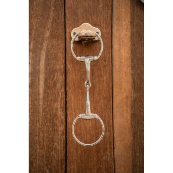 Ein glänzendes Metallpferdegebiss hängt an einer Holzwand und zeigt seine glatten Ringe und das zentrale Gelenk.