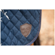 Eine Nahaufnahme einer marineblauen, gesteppten Pferde-Decke mit einem braunen Lederpatch mit dem Logo "EQUINATE" und einer Pferdesilhouette.
