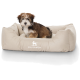 Ein kleiner, flauschiger Hund sitzt bequem in einem beigen Hundebett mit dem Logo "KNUFFELWUFF", das prominent auf der Vorderseite angezeigt wird.