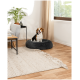 Ein Beagle sitzt glücklich in einem runden, dunkelgrauen Haustierbett auf einem Holzboden, in einem gemütlichen Wohnzimmer mit einer Pflanze und einem Couchtisch.