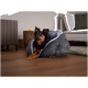 Ein kleiner Hund ruht sich bequem in einem gemütlichen, grauen Haustierbett mit weichem Innenraum aus, in einem modernen Wohnzimmer mit Holzboden und einem stilvollen Sofa.