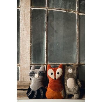 Drei plüschige Tier-Spielzeuge: ein grauer Waschbär, ein orangefarbener Fuchs und ein grauer Bär, vor einem rustikalen Fensterhintergrund ausgestellt.