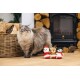 Fluffy gray tabby cat with blue eyes standing near a basket of firewood and three Christmas plush toys on a wooden floor.