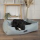 Ein schwarzer Hund, der in einem hellblauen Haustierbett mit dem Etikett "Scruff's" entspannt, in einem modernen Wohnraum mit einem Holztisch und dekorativen Pflanzen.