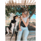 Eine Frau in einem Tanktop und Jeans sitzt auf einer Parkbank und interagiert mit einem freundlichen schwarz-weißen Hund unter einem sonnigen Himmel.