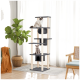Zwei Katzen, eine flauschige weiße und eine graue, sitzen auf einem hohen Katzenbaum in einem hellen Raum mit einer Pflanze und einem geflochtenen Korb.