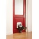 Un chat tigré émerge d'une porte pour chat PetSafe blanche installée dans une porte rouge vif, avec un sol en bois visible en dessous.