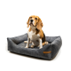Ein Beagle sitzt auf einem plüschigen grauen Hundebett mit erhöhten Rändern, mit einem kleinen braunen Etikett an der Seite.