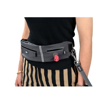 Une personne en haut côtelé noir et en pantalon rayé tient une ceinture porte-sac à déjections pour animaux grise avec deux poches zippées et un distributeur rose.