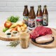 Frische Zutaten für Haustierfutter: rohes Rind- und Hühnerfleisch, Gemüse, ein Apfel, Kräuter und vier Tjure-Getränke mit den Bezeichnungen "Lamm," "Pute," "Rind," "Geflügel."