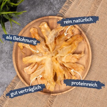 Getrocknete Haustierleckerlis in einem kreisförmigen Muster auf einem Holztablett, beschriftet mit "als Belohnung," "rein natürlich," "gut verträglich," und "proteinreich."