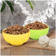Zwei bunte Schalen, eine gelbe und eine grüne, gefüllt mit Haustierfutter, stehen auf einer Juteschicht neben zwei weißen Seilspielzeugen.
