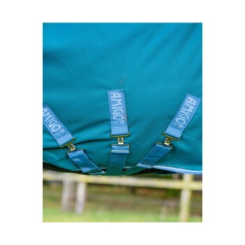 Nahaufnahme einer türkisfarbenen Pferde-Decke mit blauen Riemen mit der Aufschrift "AMIGO", die die Befestigungsklammern und die Stofftextur zeigt.