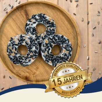 Drei runde Vogelhäuschen, gefüllt mit Sonnenblumenkernen, auf einem Holzbrett, begleitet von einem "Beste Qualität"-Abzeichen mit der Aufschrift "10 Jahre".