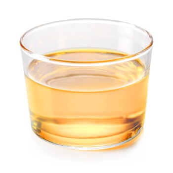 Ein klares Glas gefüllt mit einer hellen bernsteinfarbenen Flüssigkeit, die wie Haustierergänzungsöl aussieht, auf einem weißen Hintergrund platziert.