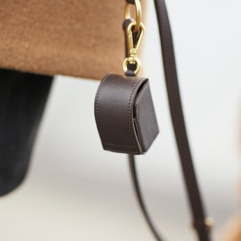 Nahaufnahme eines braunen Lederhalters für Haustierabfallbeutel, der an einem Riemen befestigt ist, mit einem goldenen Clip für eine einfache Befestigung.