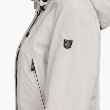 Eine Nahaufnahme einer hellbeigen Haustierjacke mit einer Reißverschlusstasche und einem Logo-Patch am Ärmel.